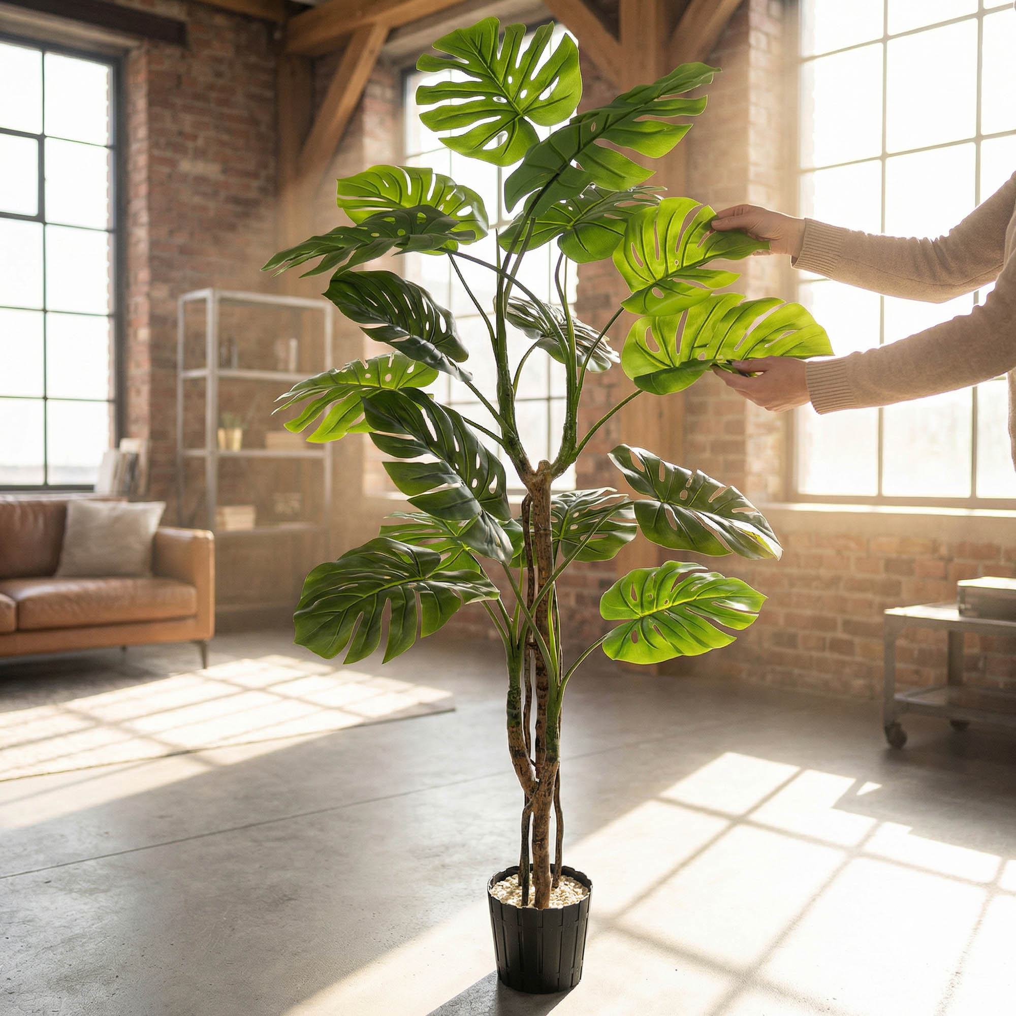 Hände richten die Blätter der künstlichen Monstera auf einem 160 cm hohen Stiel von FairyTrees aus und betonen so ihr natürliches Aussehen und ihre Flexibilität.